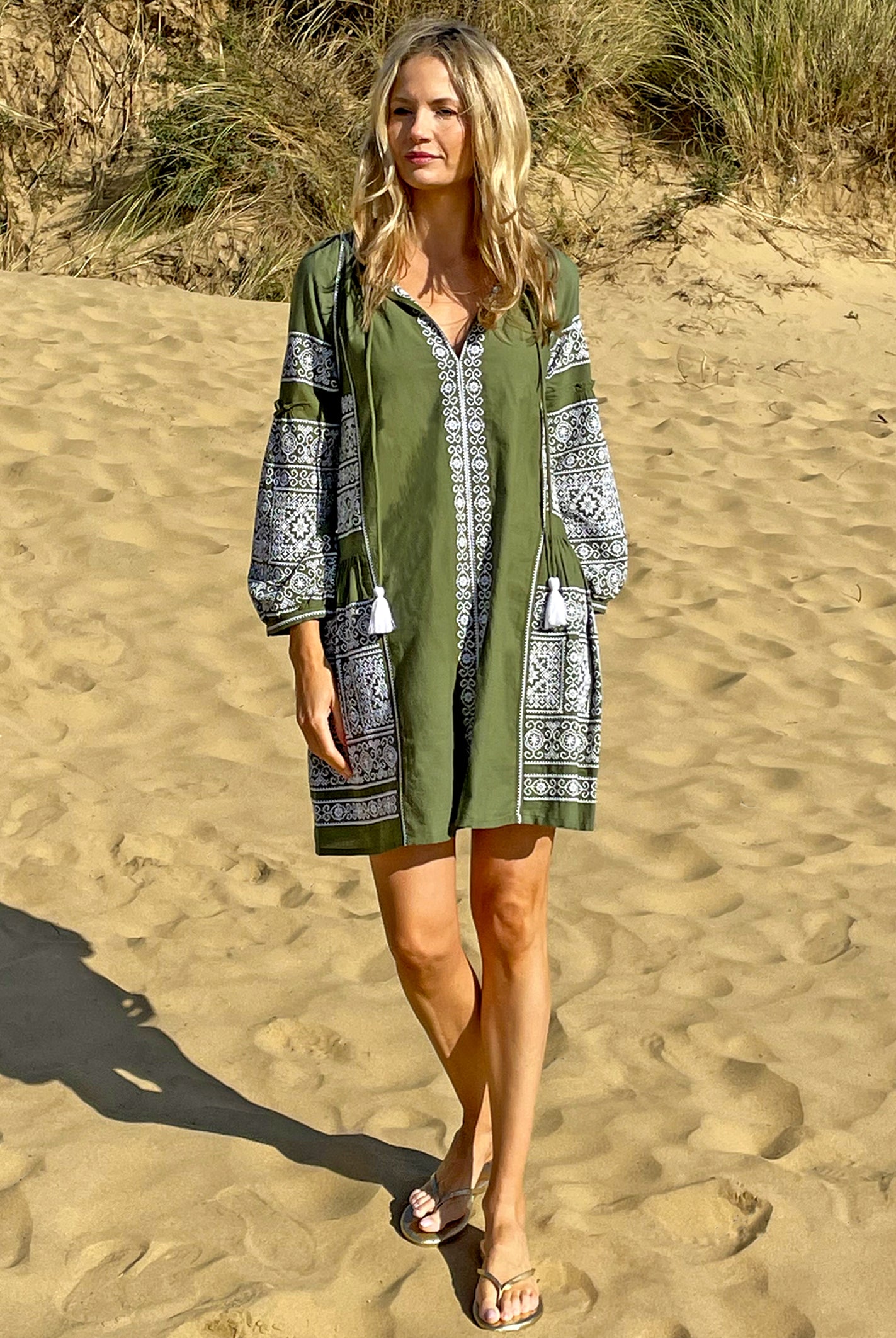 A model on a beach wearing the Rose and Rose Como embroidered dress in olive cotton.