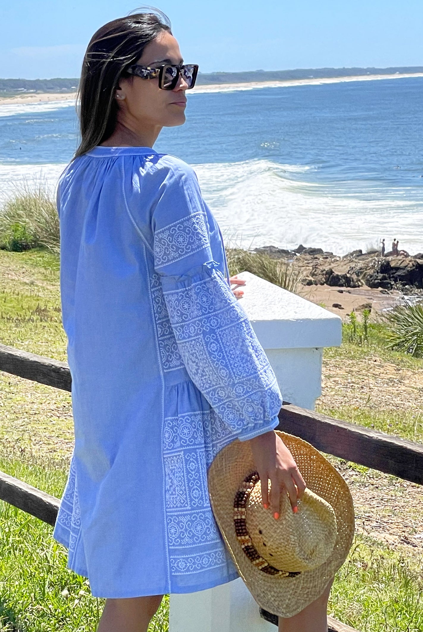 Back view of a model wearing a Rose and Rose blue Como dress and holding a hat. 