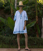 Woman wearing a white Cypress dress and straw hat standing in a tropical garden setting