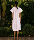 Back view of woman wearing a pale pink dress with coral trim standing in a tropical garden setting