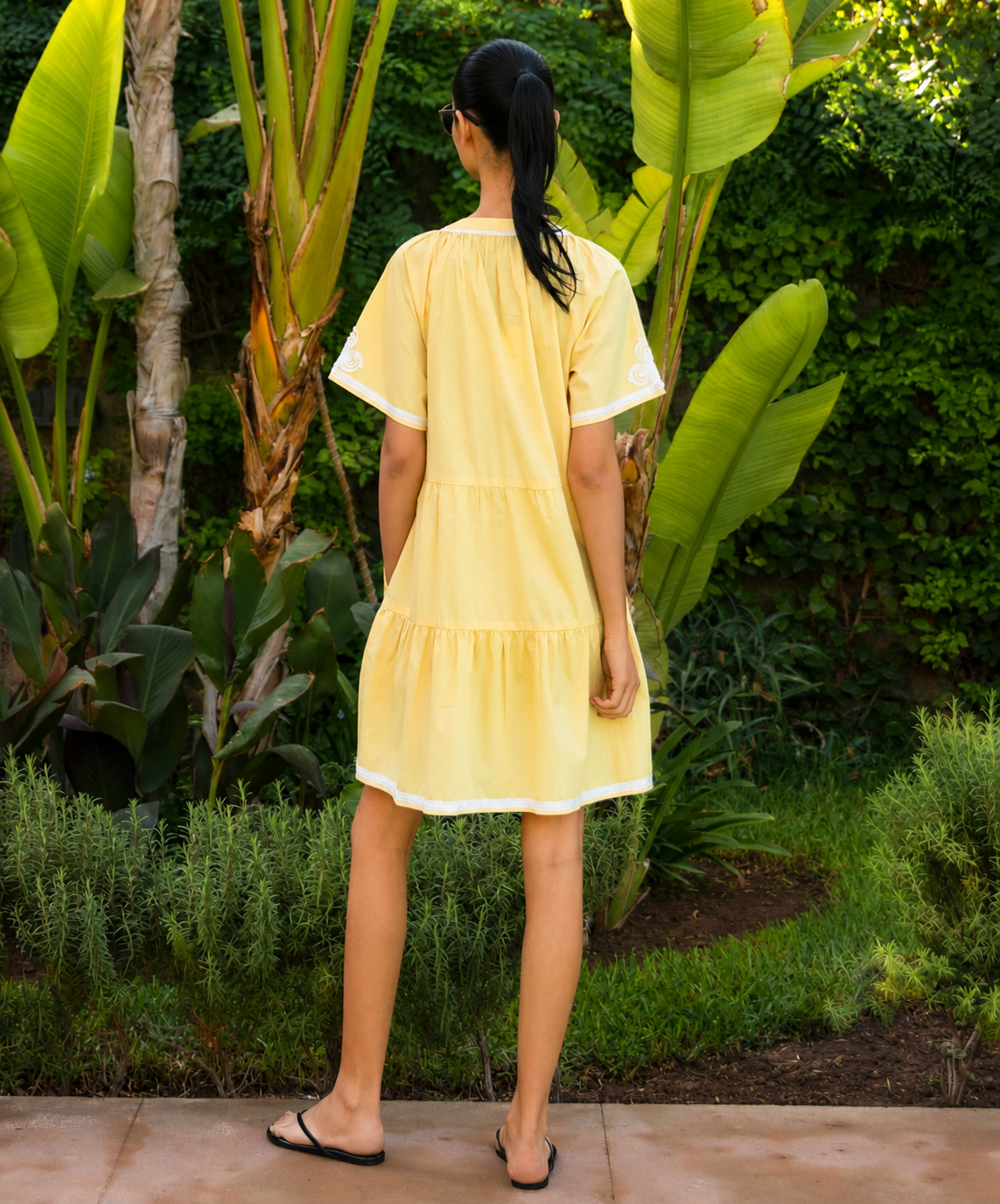 A woman wearing a yellow dress standing in a tropical garden