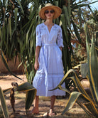 Woman in a light blue Dahlia dress and straw hat standing amongst cacti