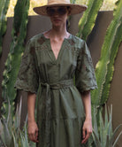 Woman wearing a green dress with embroidery details and a straw hat in front of cacti.
