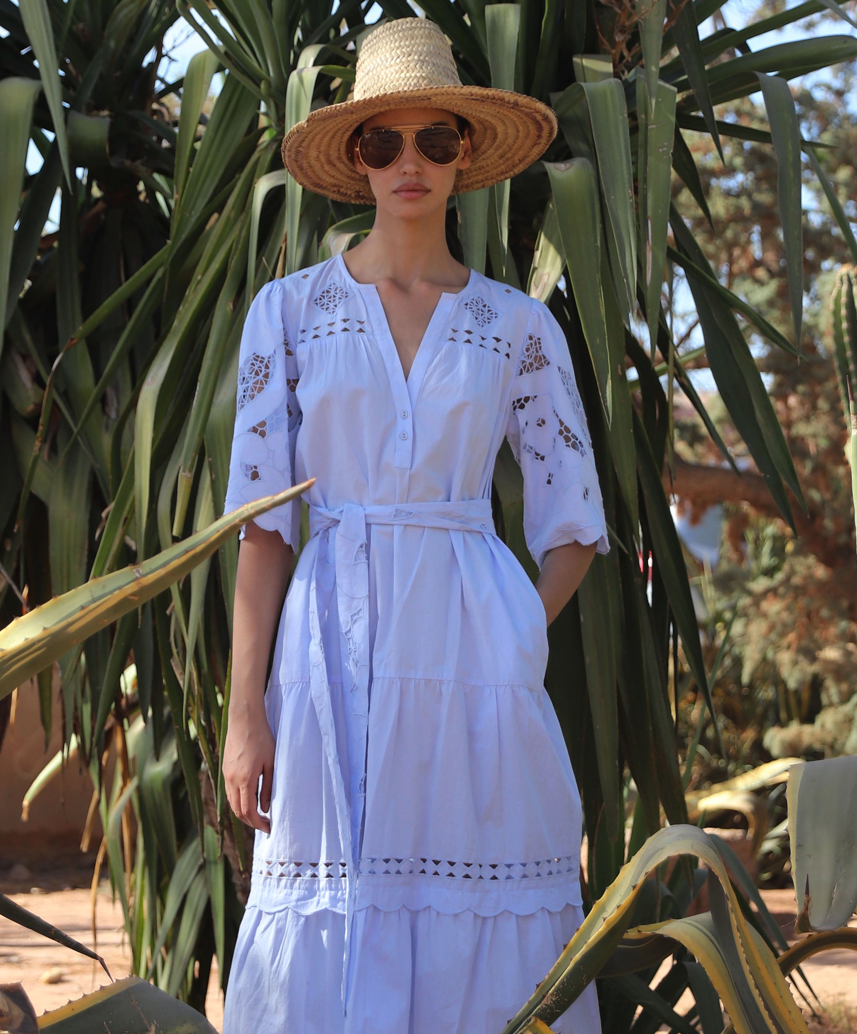 Woman in a light blue Dahlia dress and straw hat standing among cacti