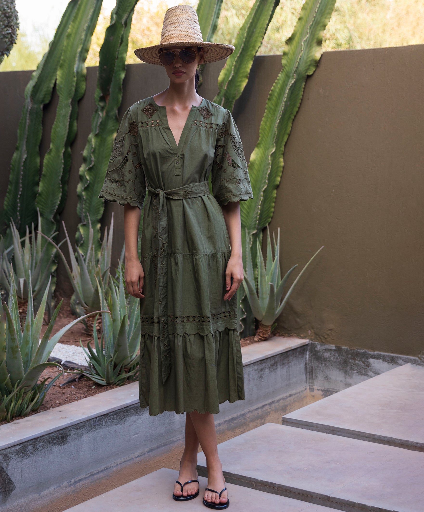 Woman in a green embroidered midi dress standing in front of cacti