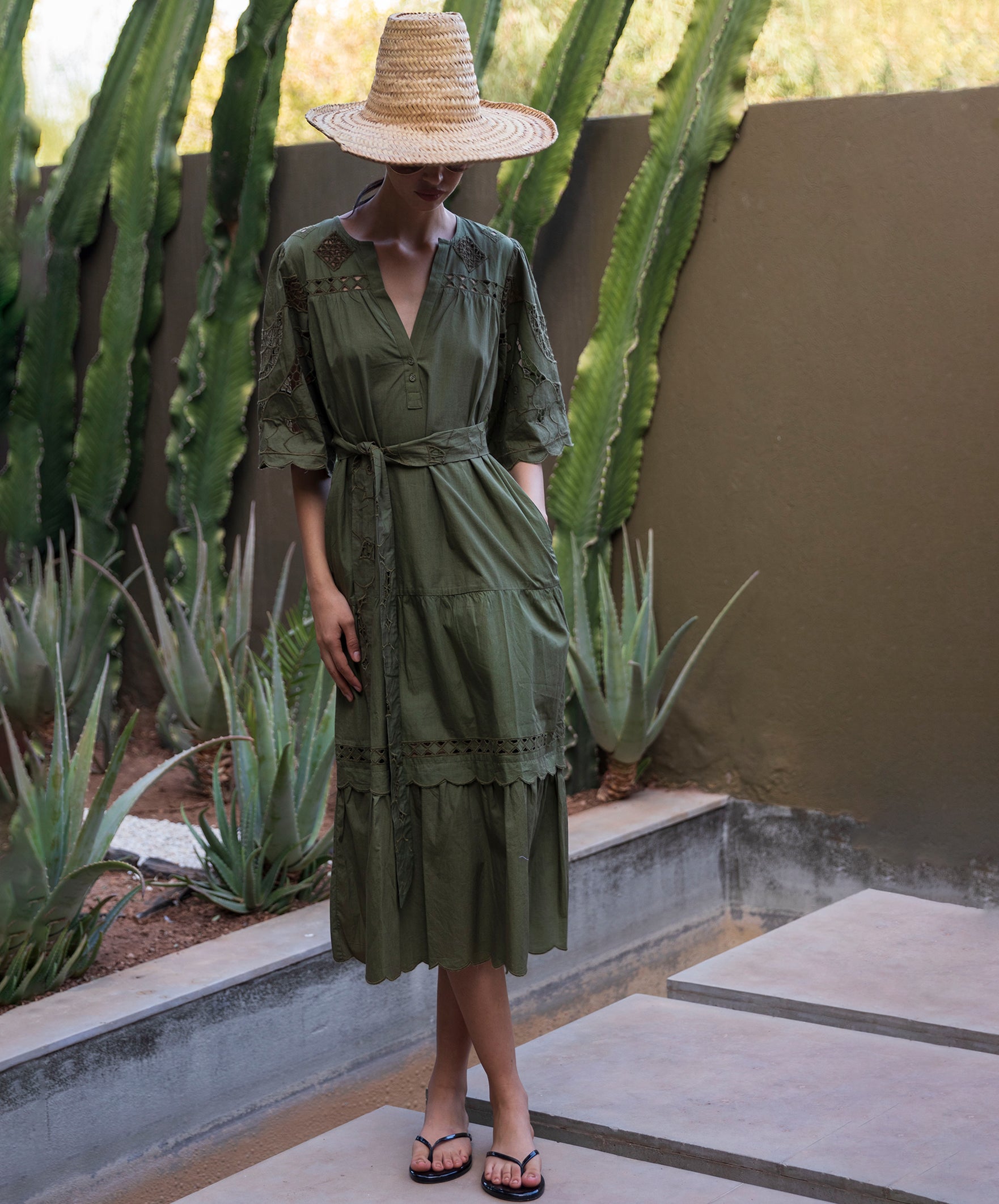 Woman in a green dress and straw hat standing in front of cacti.