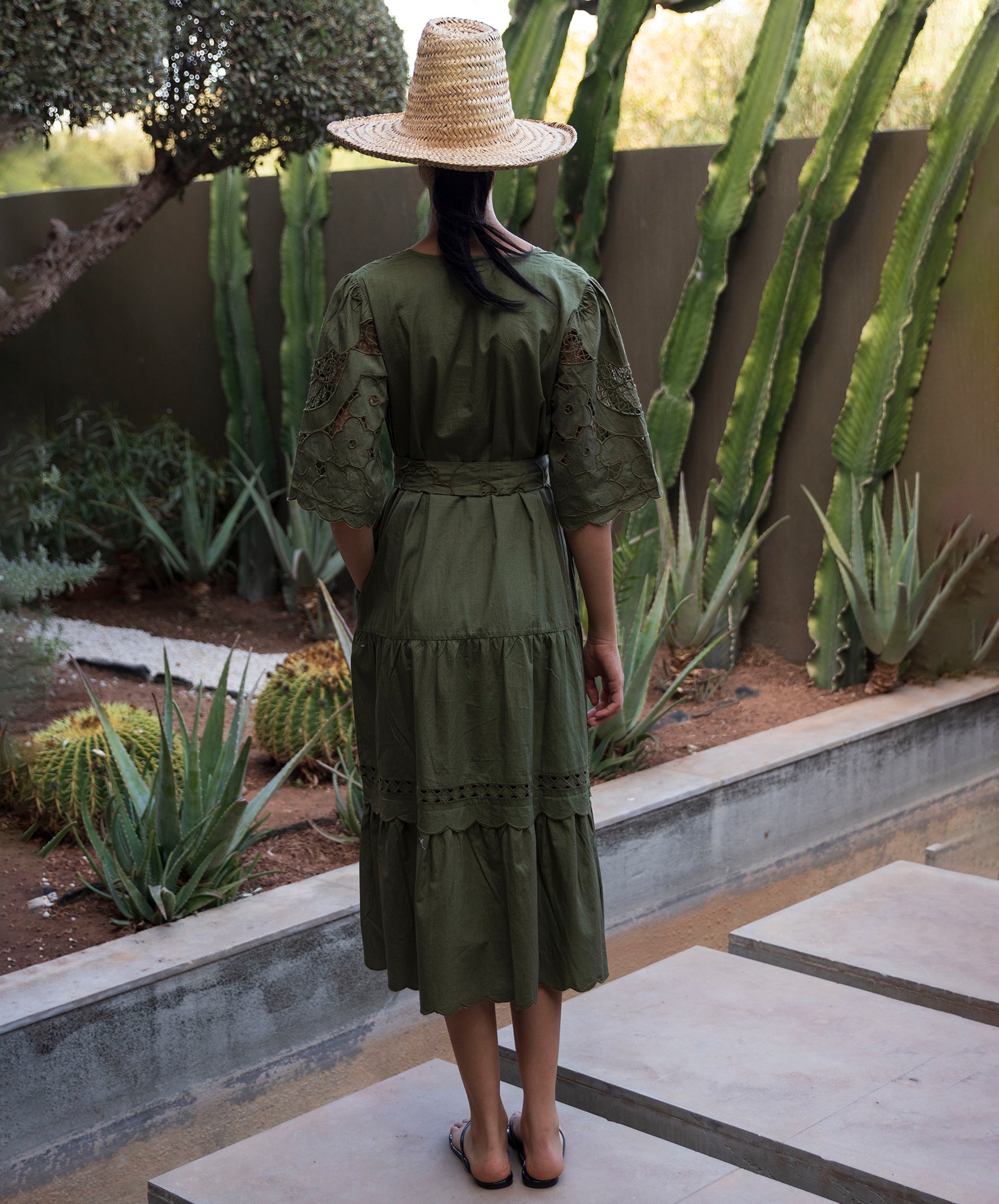 Woman wearing a green embroidered dress and straw hat standing in front of cacti