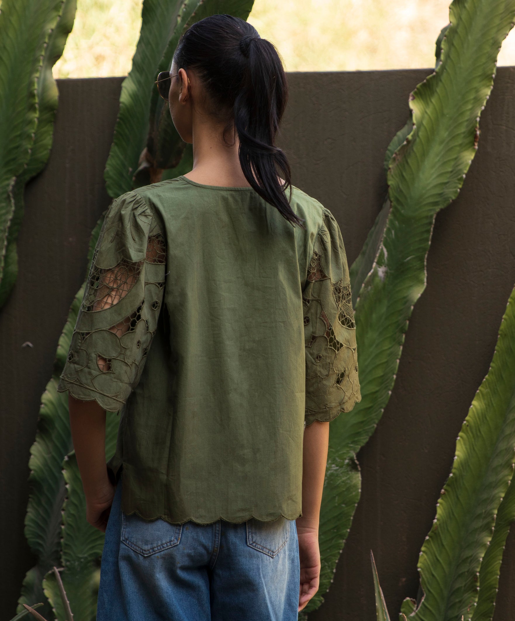 Woman wearing a green blouse with embroidered sleeves standing among cacti.
