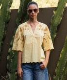 Woman wearing a pale yellow embroidered Delphinium blouse and sunglasses standing among cacti.