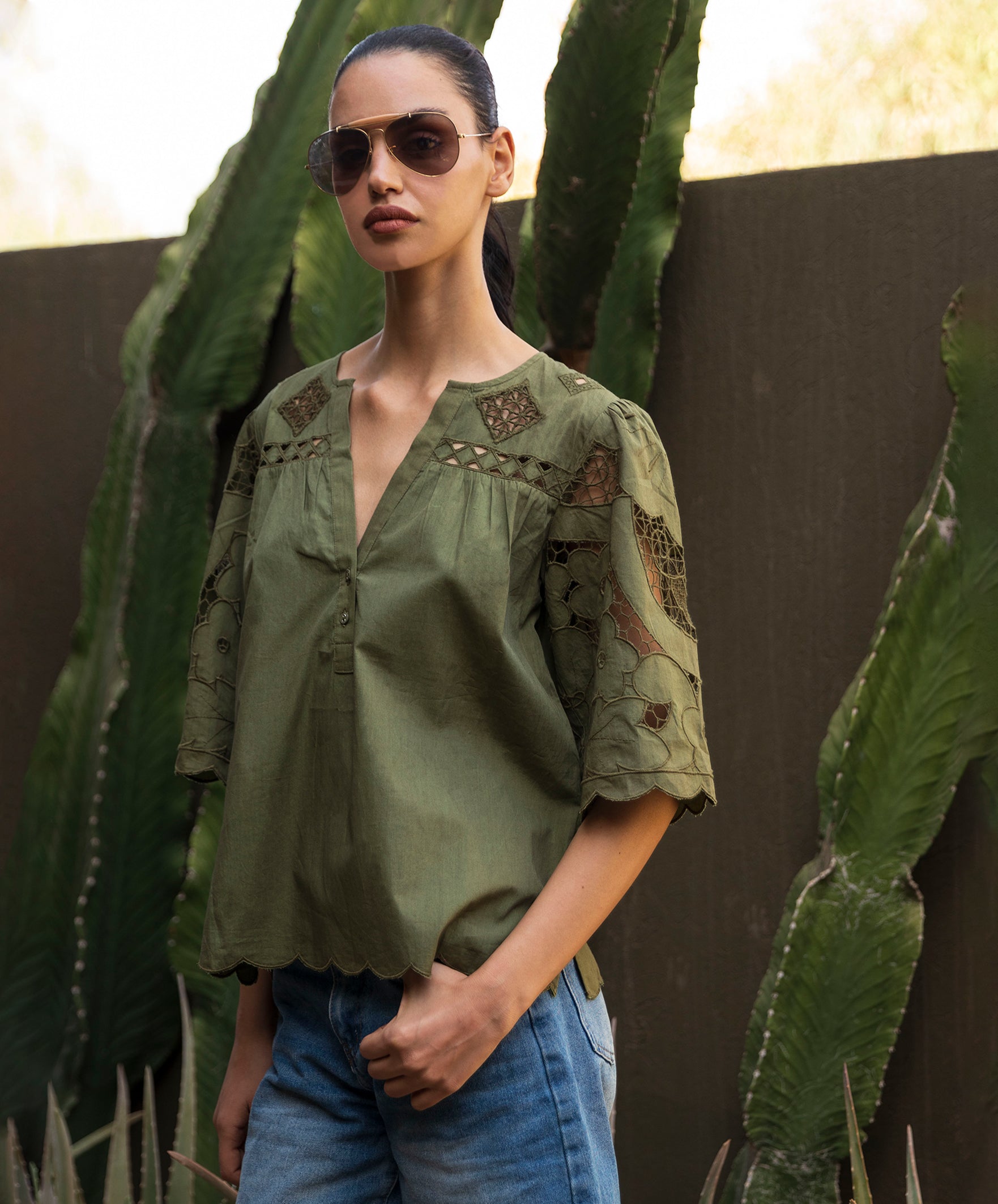 Woman wearing an olive green blouse with intricate embroidery, standing in front of cacti.