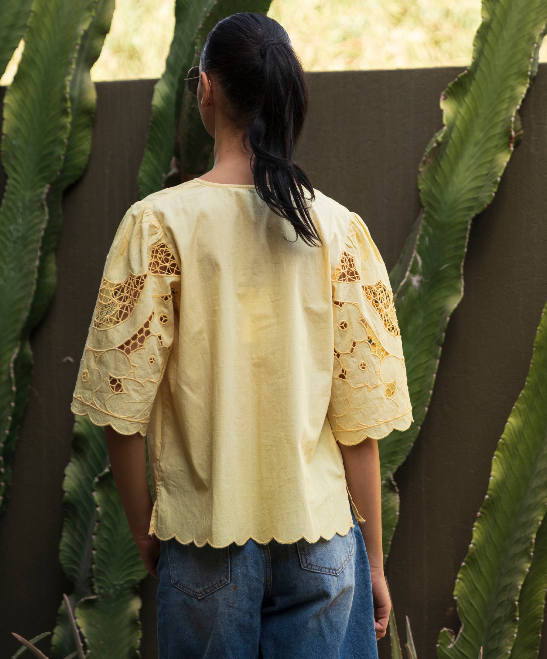 Woman wearing a light yellow Delphinium blouse with embroidered details, standing among cacti.