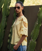Woman wearing a light yellow Delphinium blouse with embroidery details in front of cacti.
