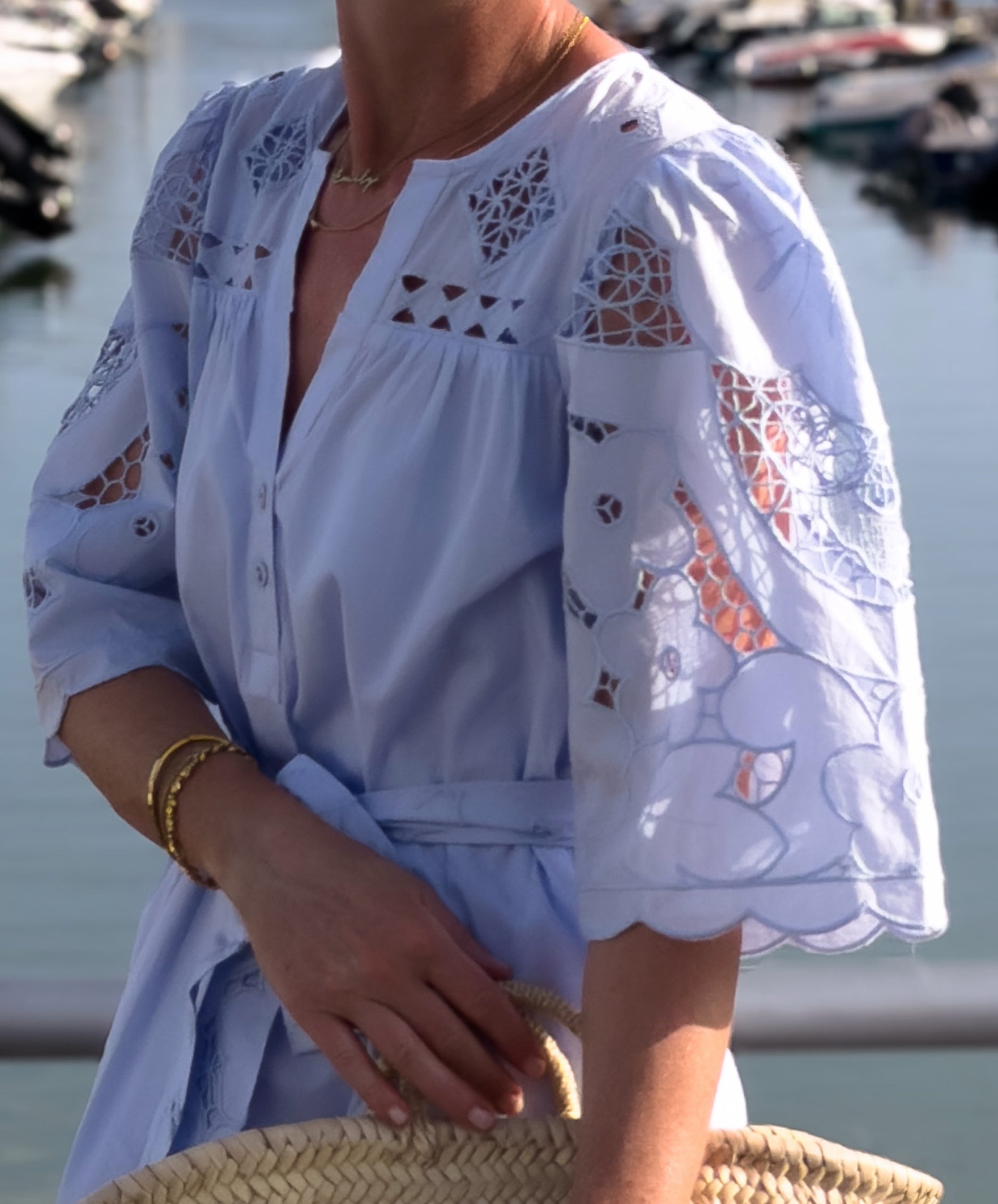 Woman wearing a light blue dress with embroidery details by a waterfront.