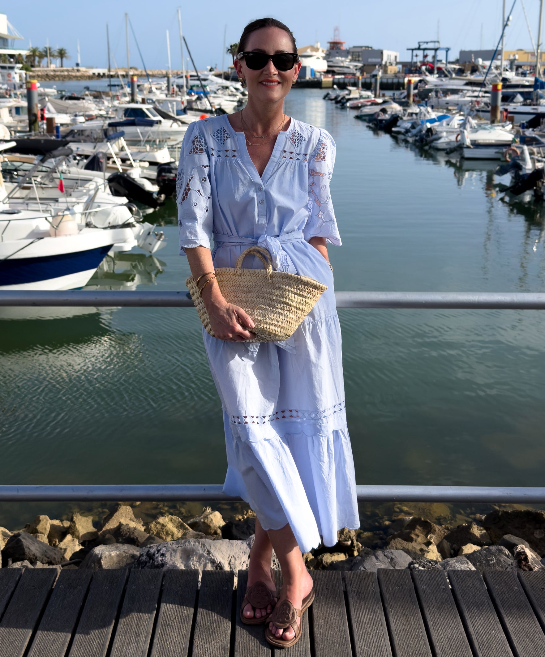 Woman in a light blue dress standing on a dock with boats in the background