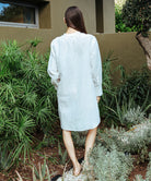 A back view of a model stood in a garden wearing a Rose and Rose Euston white linen tunic shirt.