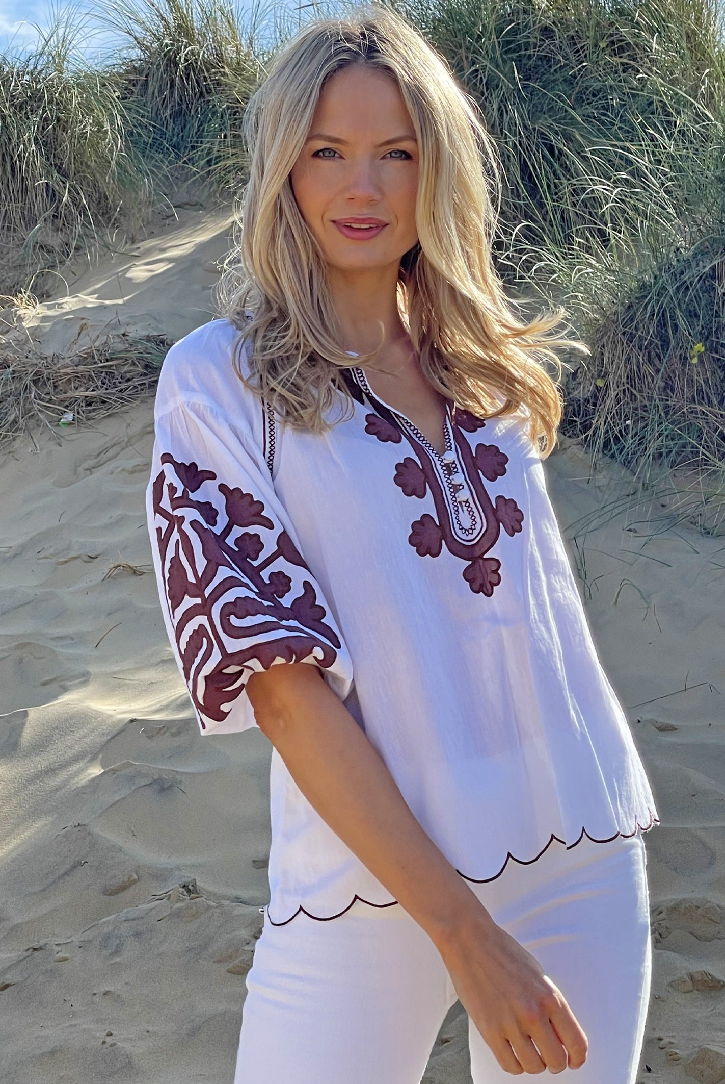 A model on a beach wearing the Rose and Rose Ferrara top in white cotton with bitter chocolate applique.