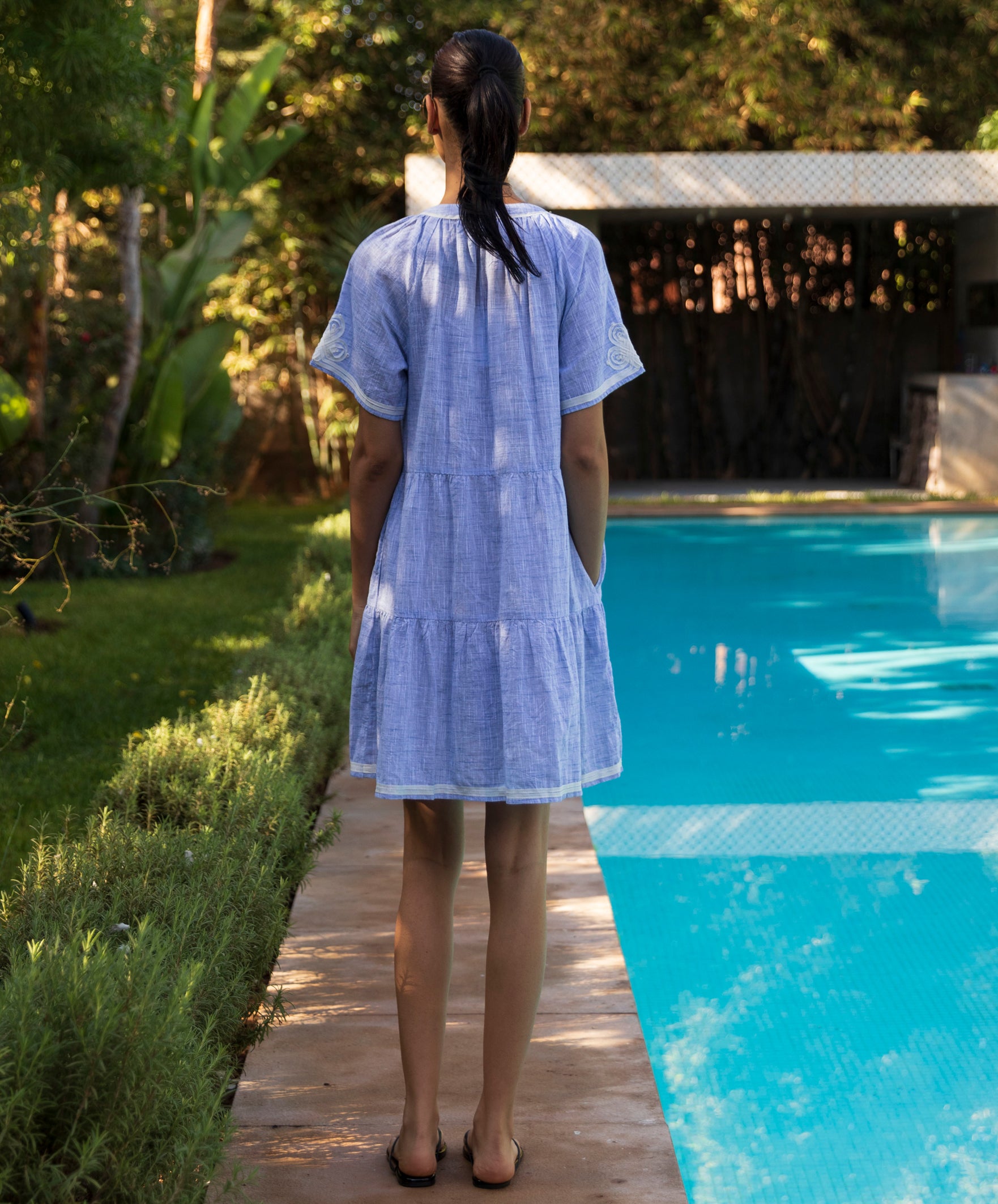 Back view of a woman in a light blue Flora dress standing by a pool 