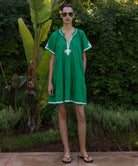 Woman wearing a green Flora dress with white passementerie decoration standing in a tropical garden setting.