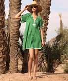 Woman in a green Flora dress and straw hat standing among palm trees.