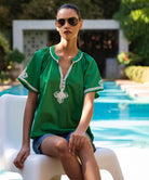 Woman in a green Foxglove top with passementerie decoration sitting by a pool