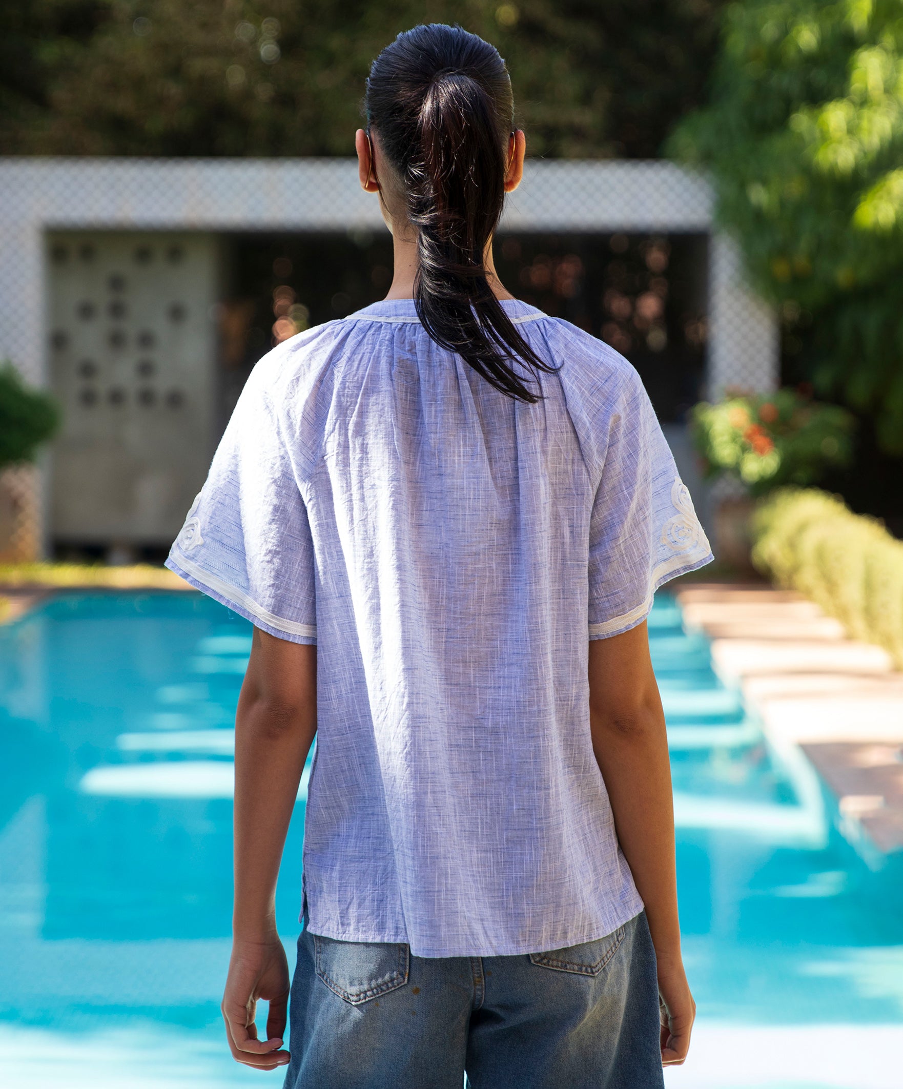 Woman wearing a light blue Foglove blouse by a pool 