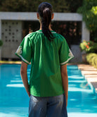 Woman wearing a green Foxglove blouse with passementerie decoration by a pool