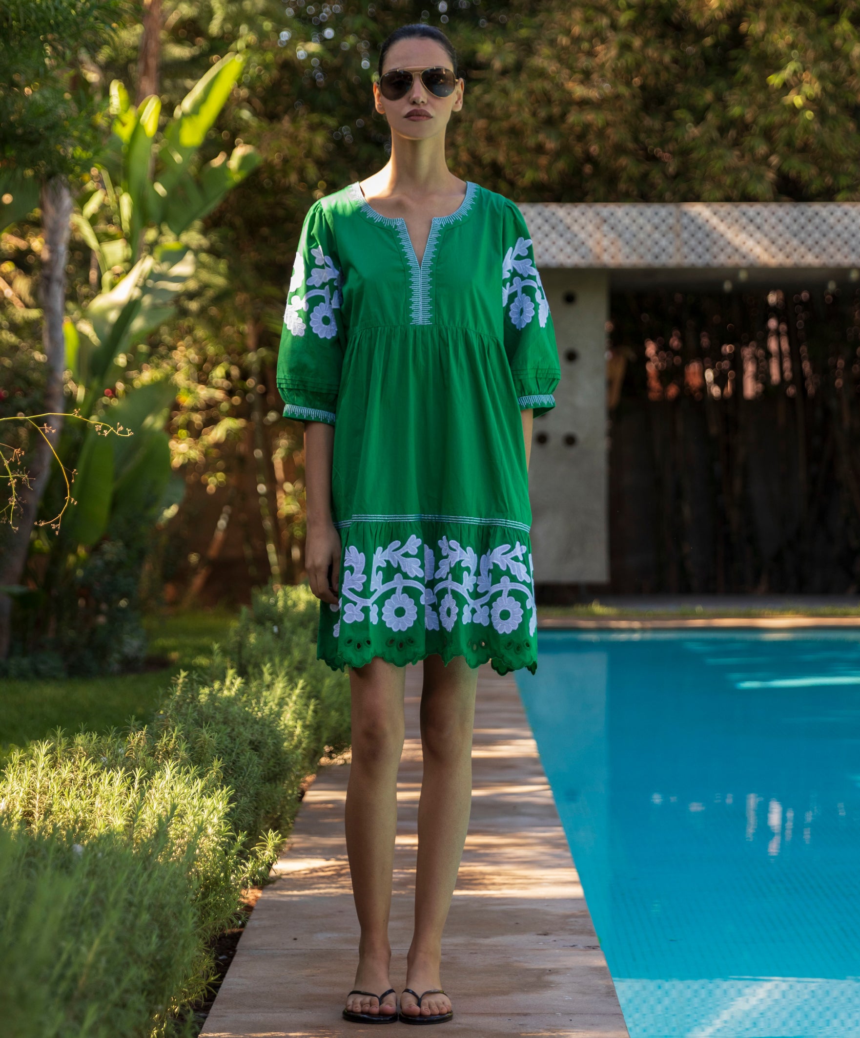 Woman in a green Genta dress with white floral patterns standing by a poolside.