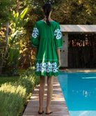 Woman in a green Genta dress with white applique standing by a poolside.