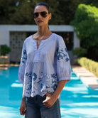 Woman wearing a light blue blouse with blue floral embroidery by a pool