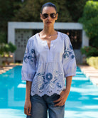 Woman wearing a light blue embroidered blouse with floral patterns by a poolside.