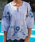 Light blue blouse with floral embroidery worn by a woman by a pool.