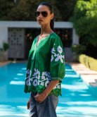 Woman wearing a green blouse with white floral patterns by a pool