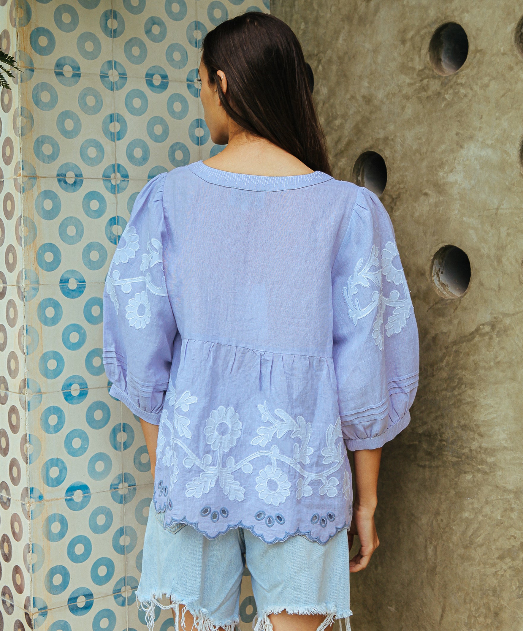 A back view of a model wearing a Rose and Rose Goldhawk decorative top in blue linen.