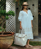 A model wearing a Rose and Rose Grange dress in White with sand appliqué decoration, a summer cotton canvas bag and a straw hat.