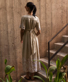 Woman in a long, natural linen dress standing on a staircase with a textured wall background