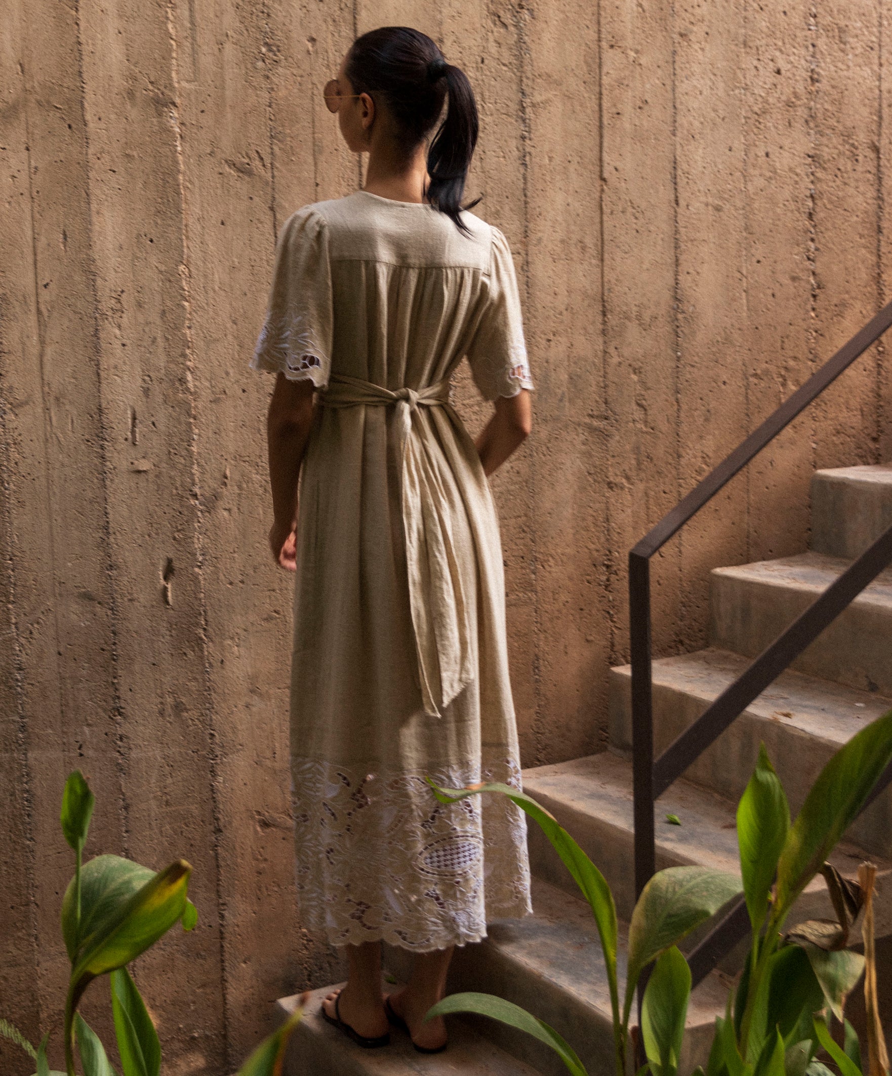 Woman in a long, natural linen dress standing on a staircase with a textured wall background