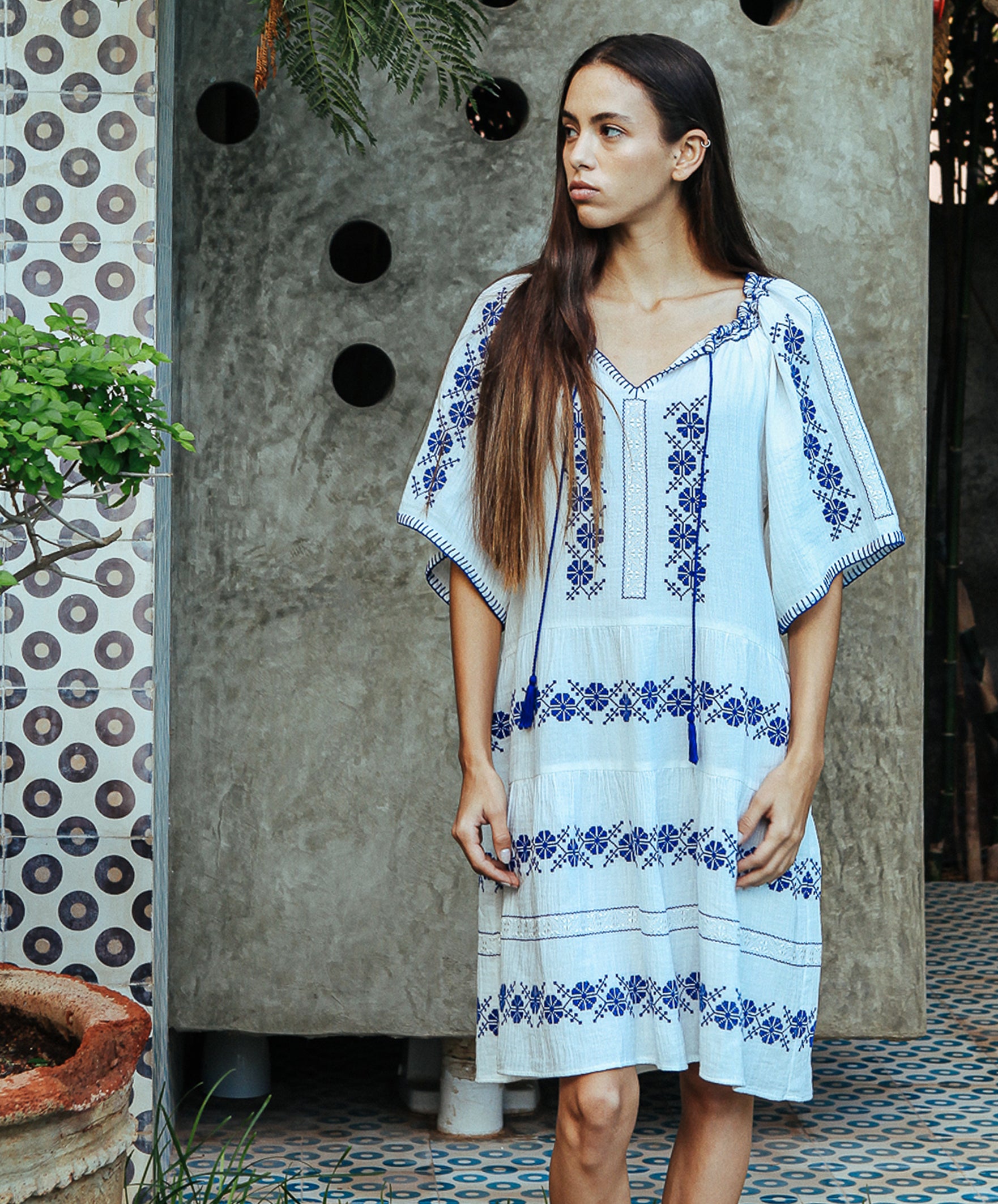 A model wearing a Rose and Rose Holborn  cotton dress in white with cobalt blue embroidery. 