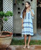 A model wearing a Rose and Rose Holborn  cotton dress in white with cobalt blue embroidery. 