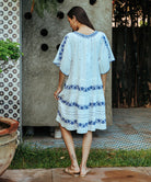 A back view of a model wearing a Rose and Rose Holborn  cotton dress in white with cobalt blue embroidery. 