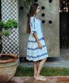 A side view of a model wearing a Rose and Rose Holborn  cotton dress in white with cobalt blue embroidery. 