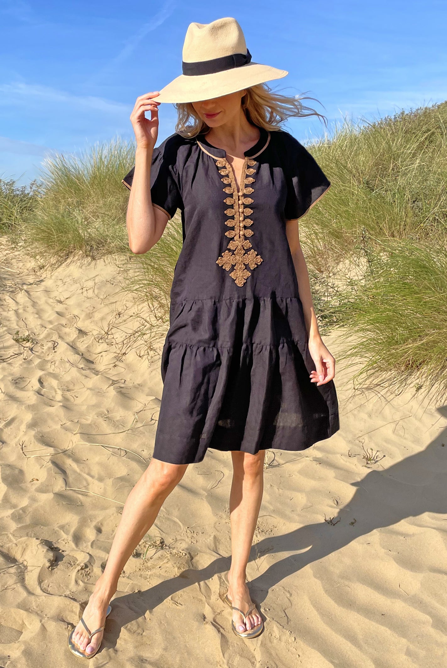 A model on a beach wearing the Rose and Rose Ischia dress in black cotton and an Anthony Peto Panama hat.