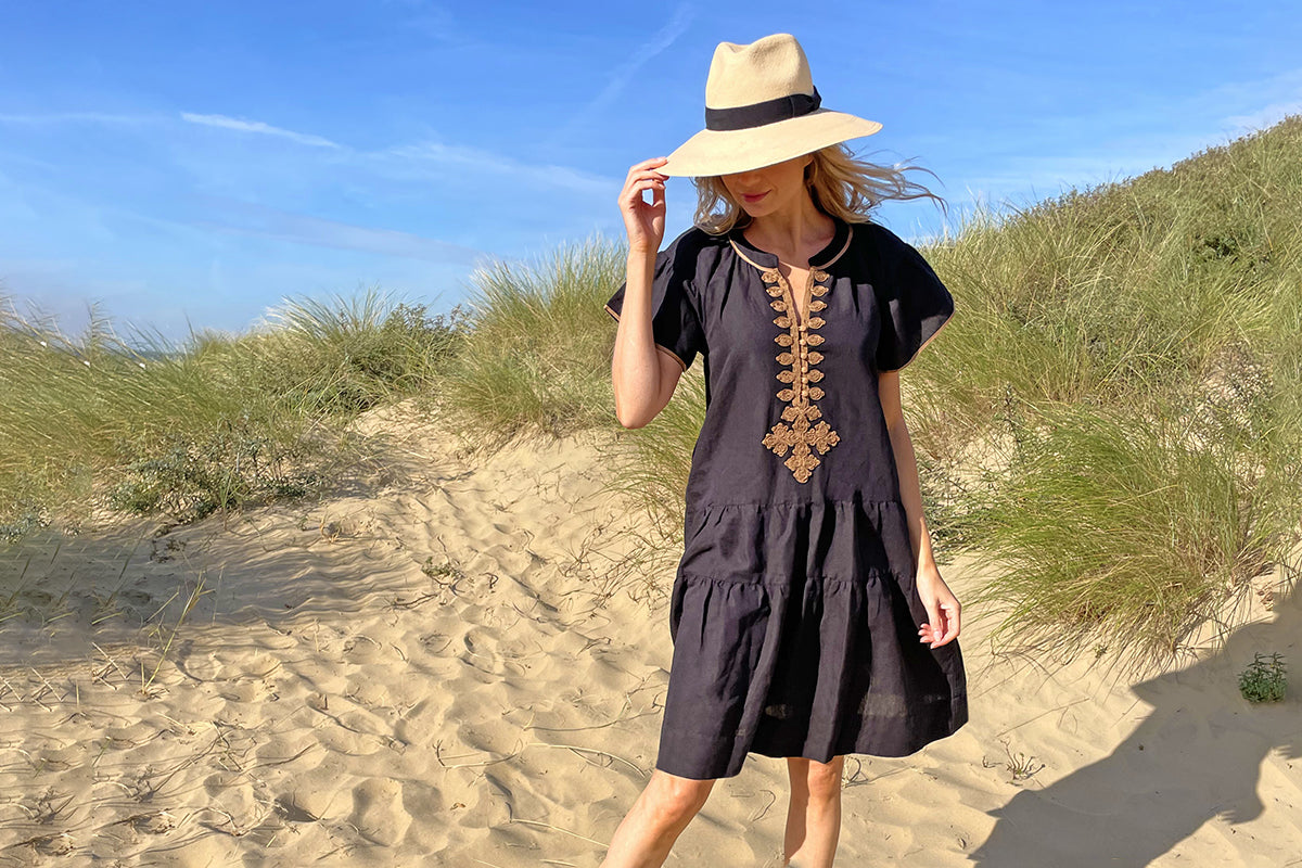 A model on the sand dunes wearing a Rose and Rose black cotton Ischia dress and Panama hat. 