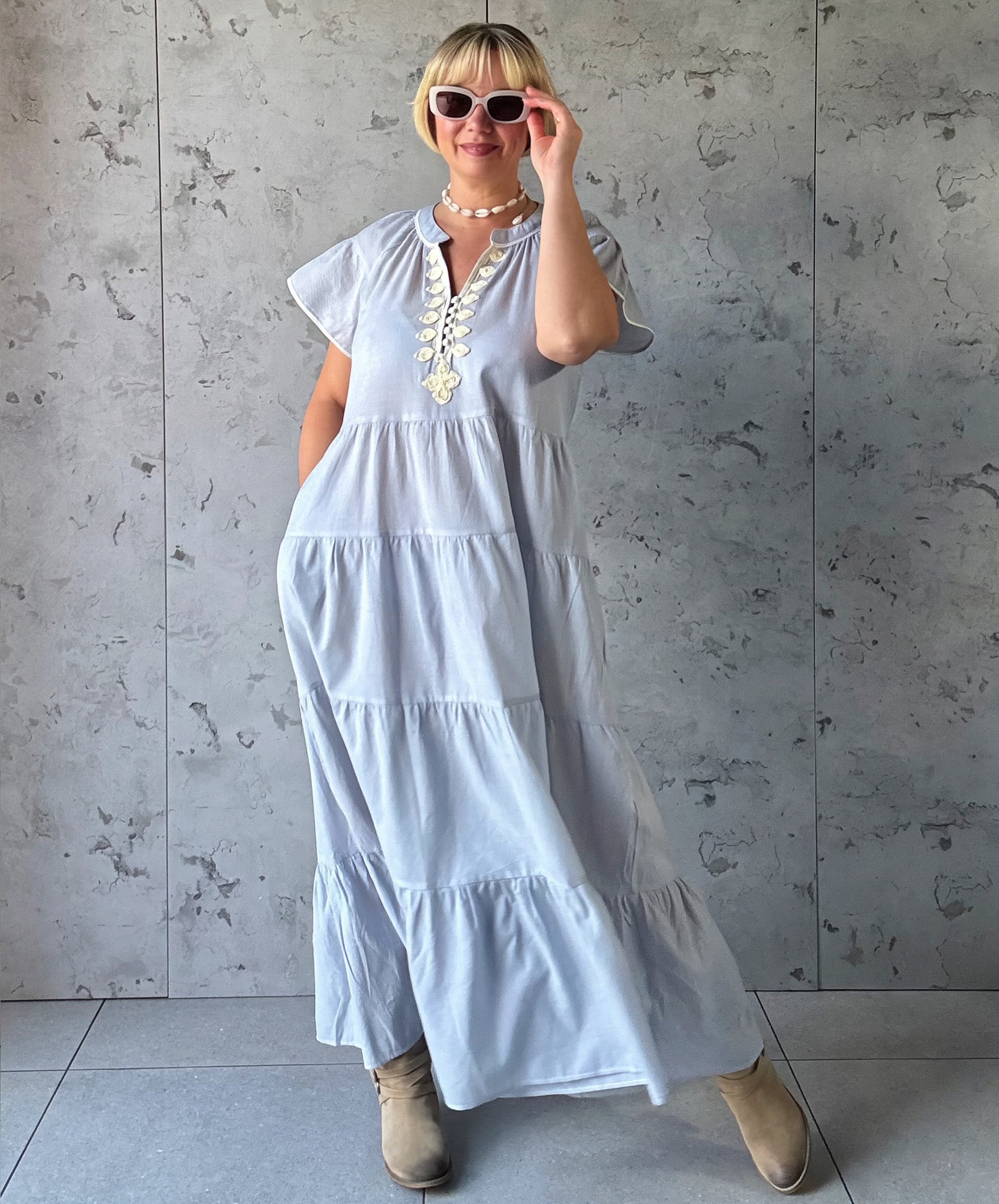 Woman wearing a blue striped dress against a gray concrete wall.
