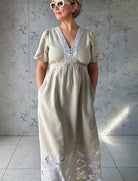 Influencer @rosemaejewel wearing a Hawthorn natural dress with her hands in the pockets against a gray concrete wall.