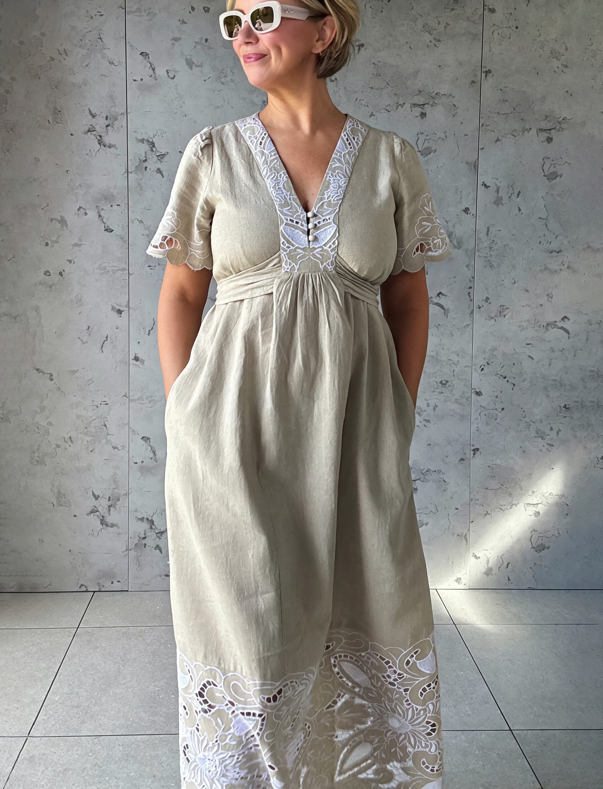 Influencer @rosemaejewel wearing a Hawthorn natural dress with her hands in the pockets against a gray concrete wall.