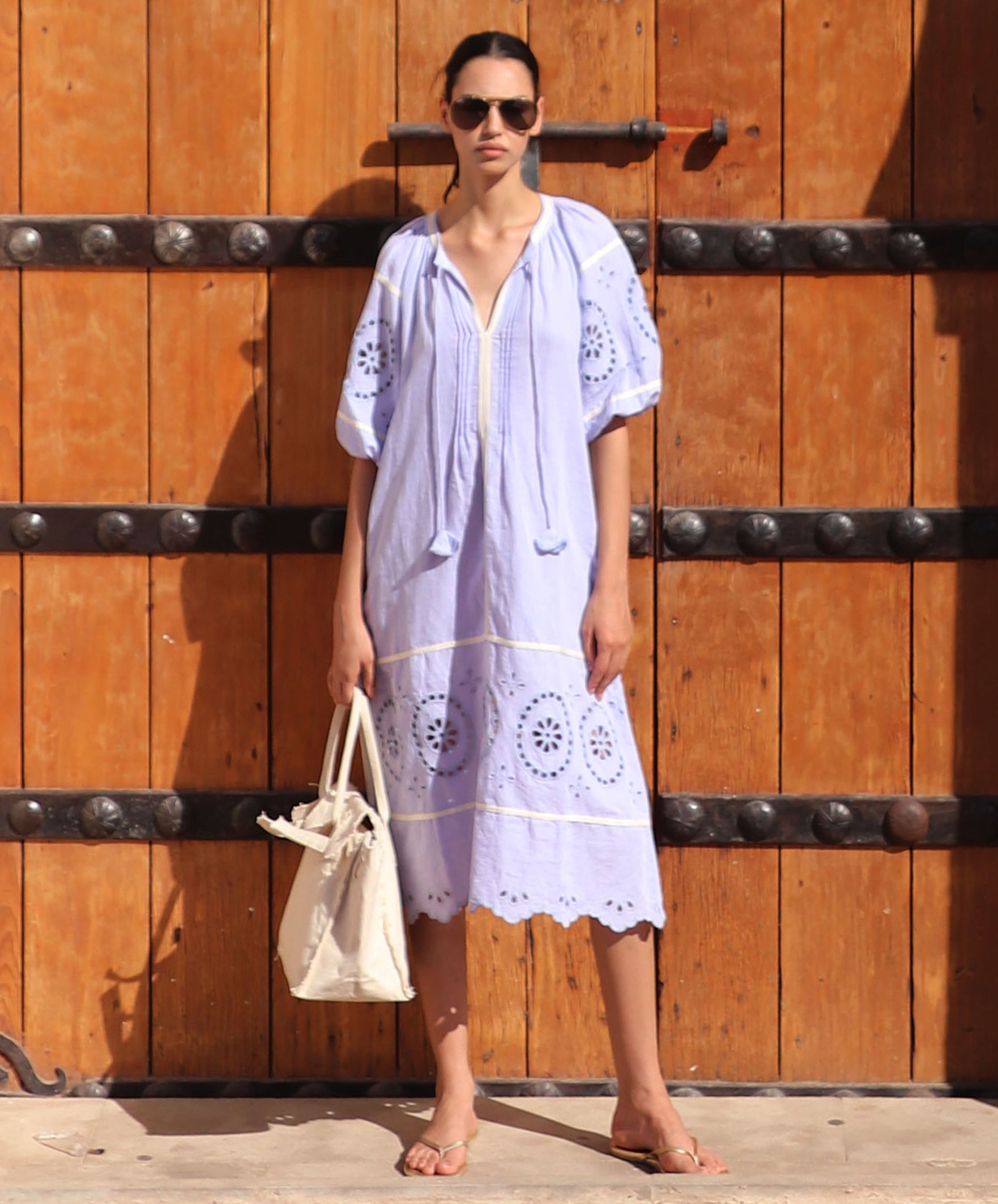 Woman in a light blue embroidered dress standing in front of a large wooden door.