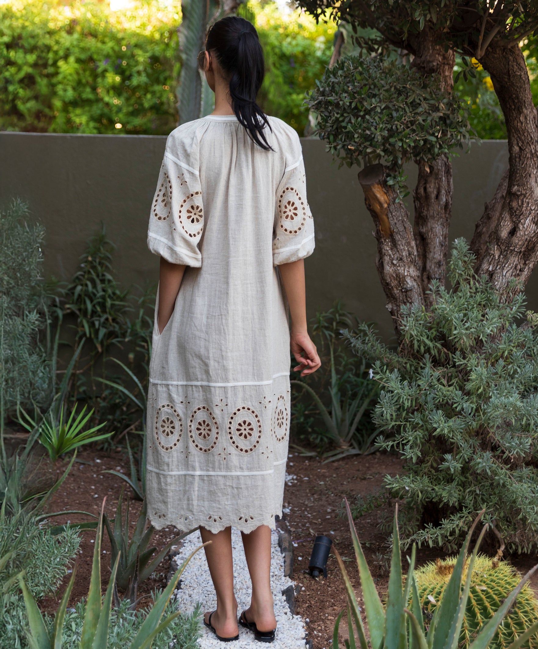 Woman in a natural linen dress with embroidery details standing in a garden.