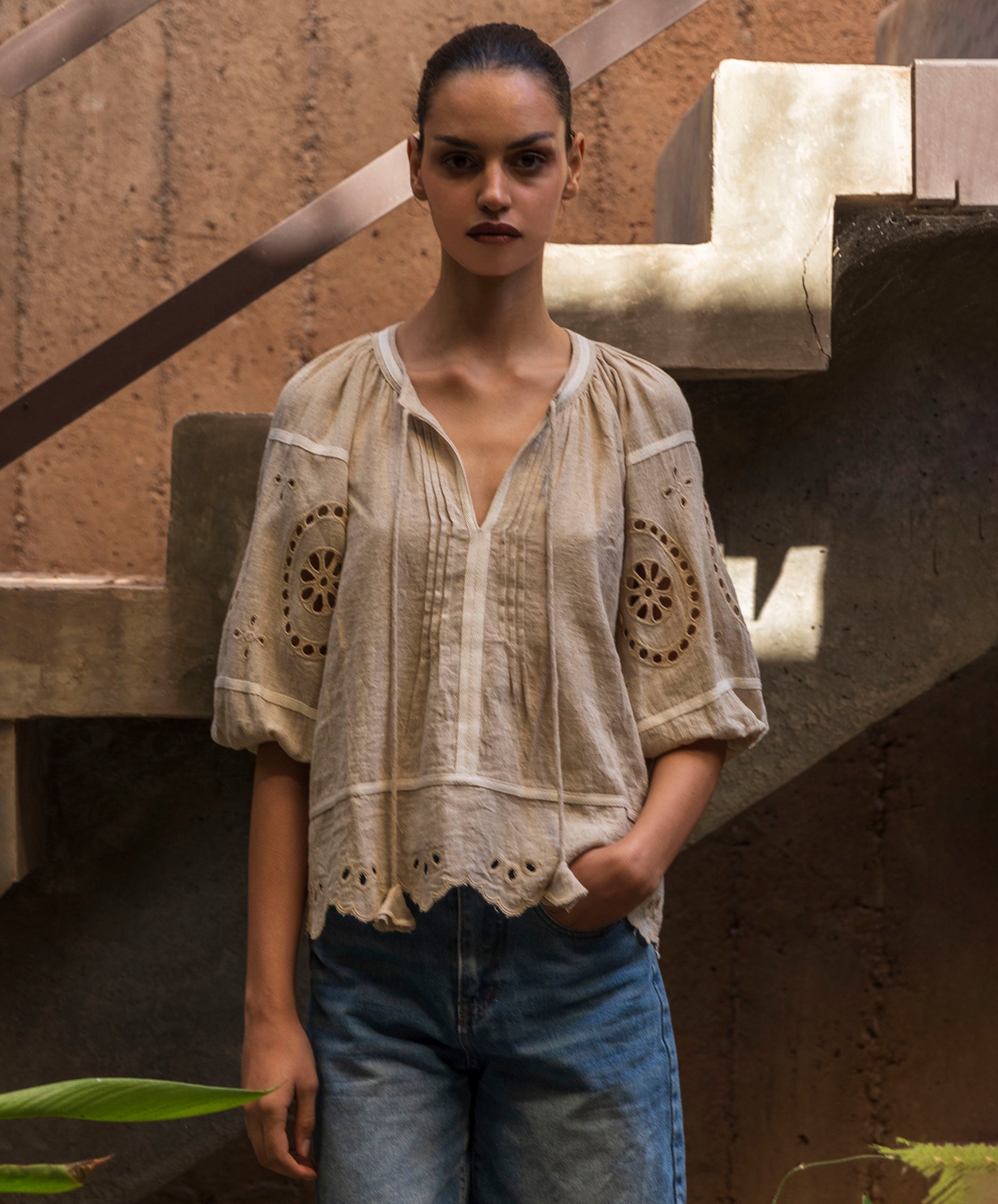 Woman wearing a natural linen embroidered blouse and blue jeans standing in a rustic setting.