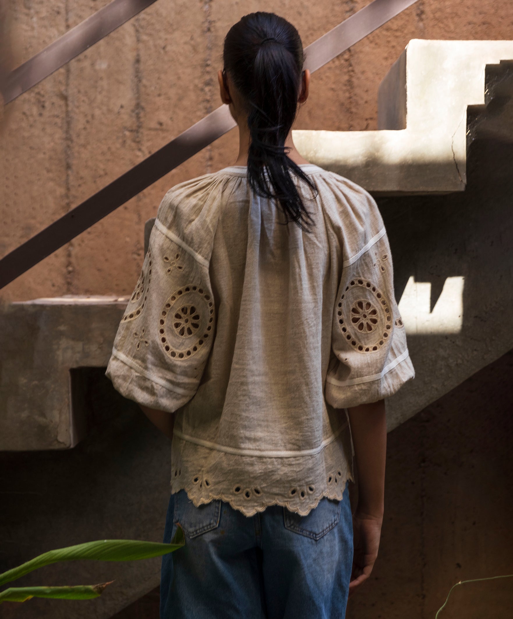 Woman wearing a natural linen blouse with intricate embroidery standing on a staircase.