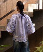 Woman wearing a light blue embroidered blouse in an outdoor setting.